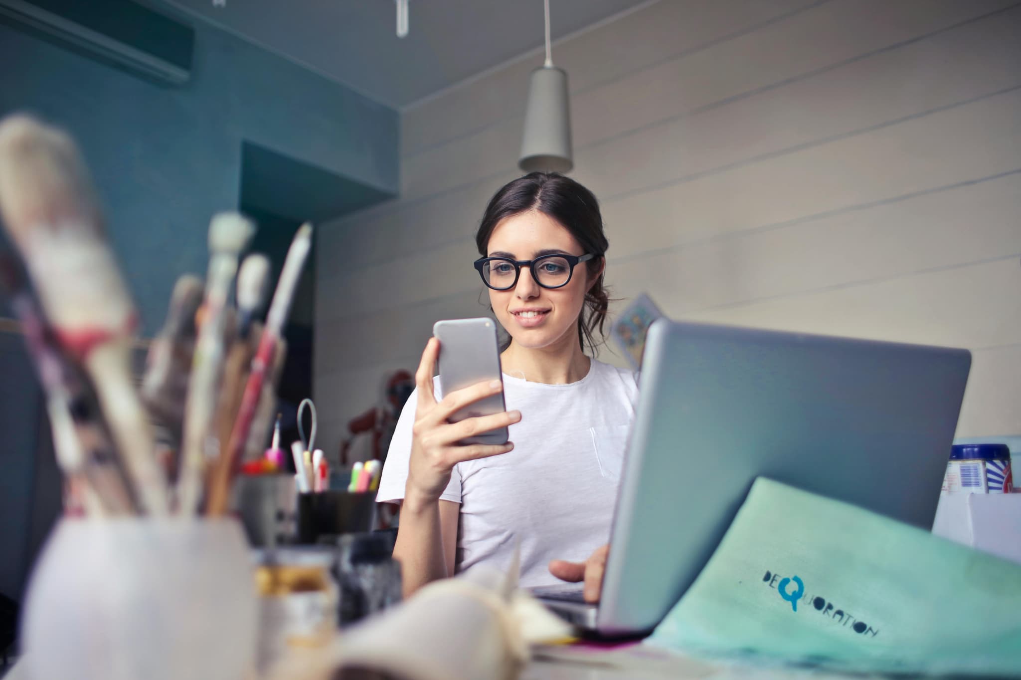young business woman looking at phone while sitting at a desk with a laptop