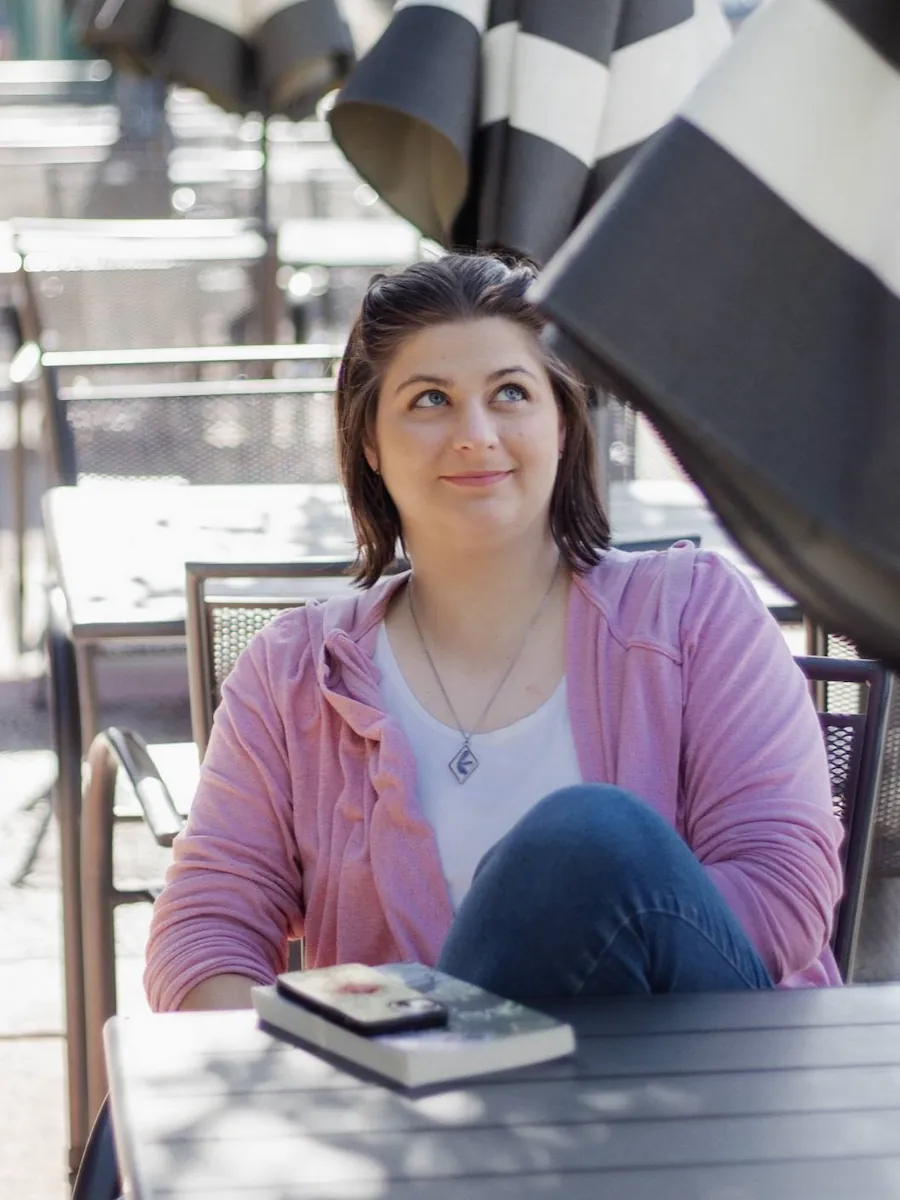 Mandy sitting at an outdoor cafe table, 'My World of Glass' on the table