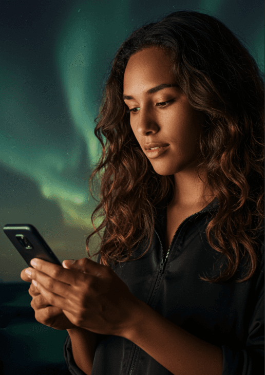 Woman looking down at phone checking her business increase after SEO from Elevation Tech with the aurora lights in the background.